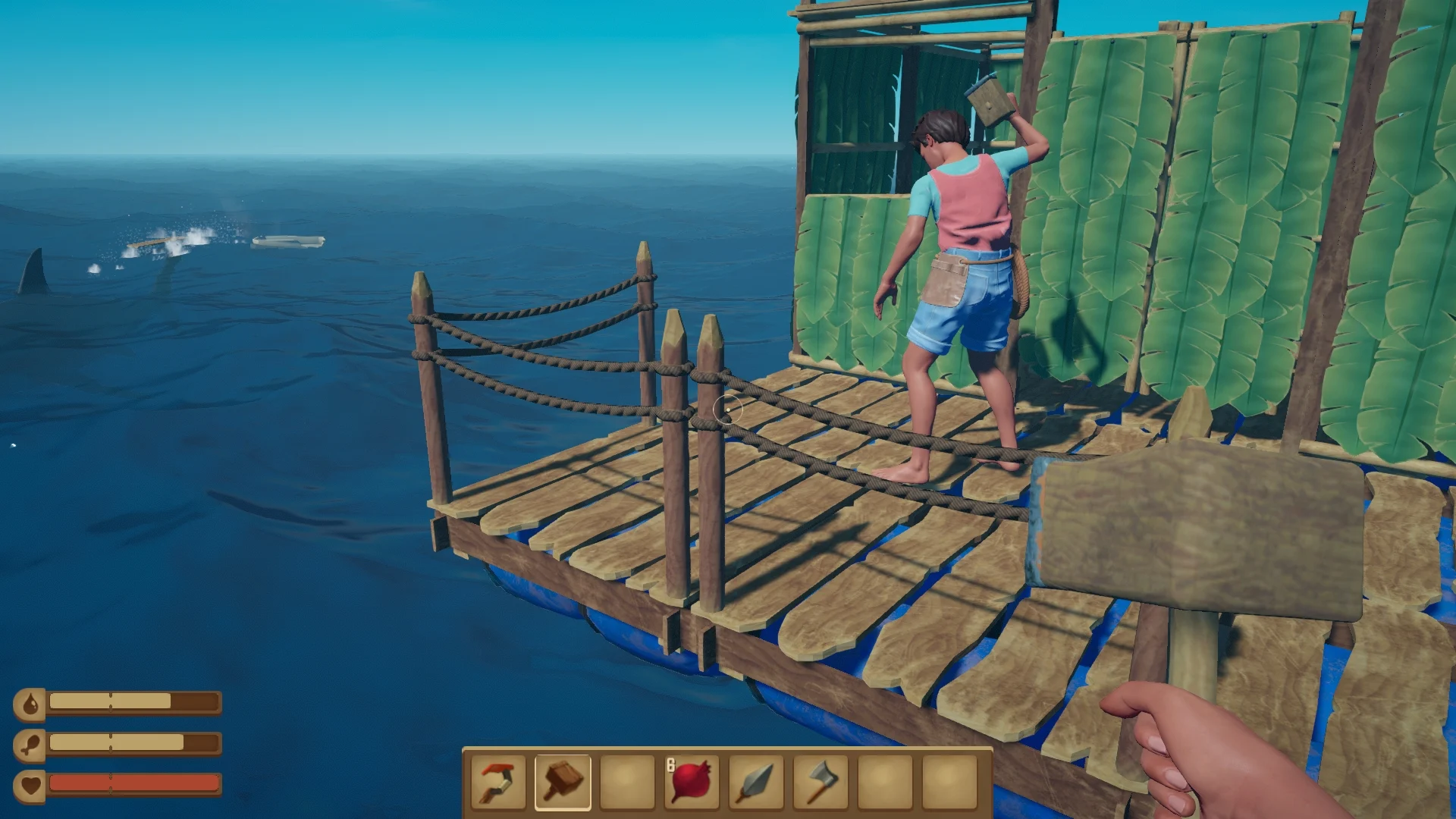 A first-person view in the game Raft, showing a multi-level wooden raft constructed on the open blue ocean. Another character stands on deck, which has green bamboo walls. A shark fin breaks the surface of the water in the distance. The player's hand, holding a hammer, is visible in the foreground.