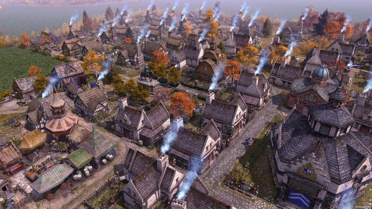 An aerial, slightly elevated view of a bustling town in Farthest Frontier during autumn. Many houses with smoking chimneys are clustered together on dirt roads, surrounded by colorful fall trees and a glimpse of a body of water in the background.