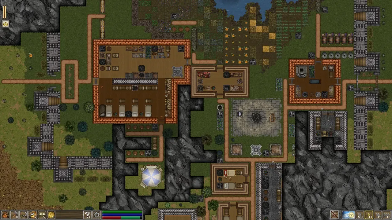 A top-down view of a detailed medieval settlement in First Feudal, showing a collection of multi-room buildings with open interiors, various workshops, farm plots, and paths connecting them, all nestled between rocky terrain and a body of water.